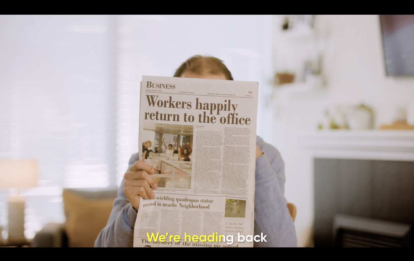 Screen grab from a video showing a man reading a newspaper with the headline "Workers happily return to the office"